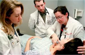 Doctor examines a patient while two medical students observe
