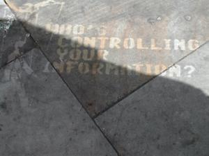 Photo of graffiti on the ground that says "Who's controlling your information?"