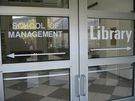 Photo of glass door with School of Management to the left and Library to the right