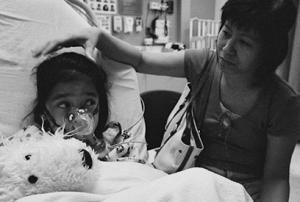 child wears a respirator in a hospital bed while woman looks on