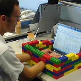 Person typing on laptop with Lego wall around it