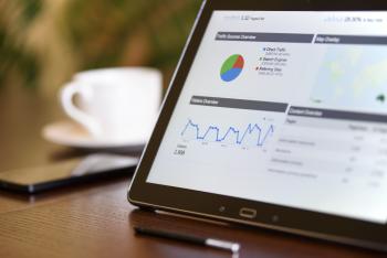 A pie chart and a line graphs on a tablet computer screen next to a cup of coffee