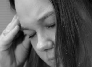 black and white image of woman holding hand to temple with eyes closed