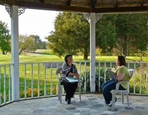 Two women sitting in chairs in an outdoor gazebo