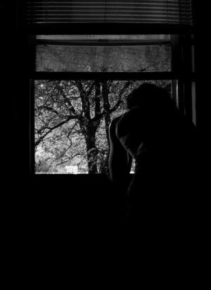 black and white image of woman facing away from camera looking out a window at a tree
