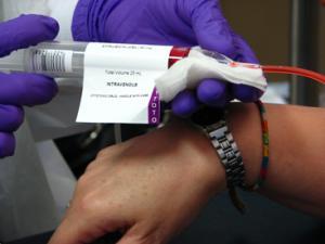 gloved hands hold tube of blood attached to person's arm