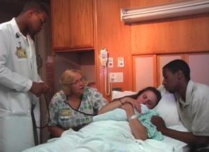 patient holds newborn in hospital bed while hospital staff looks on